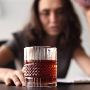 Девушка сидит и смотрит на стакан с алкоголем