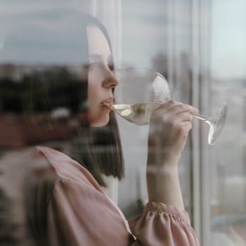 Девушка смотрит в окно и пьет из бокала